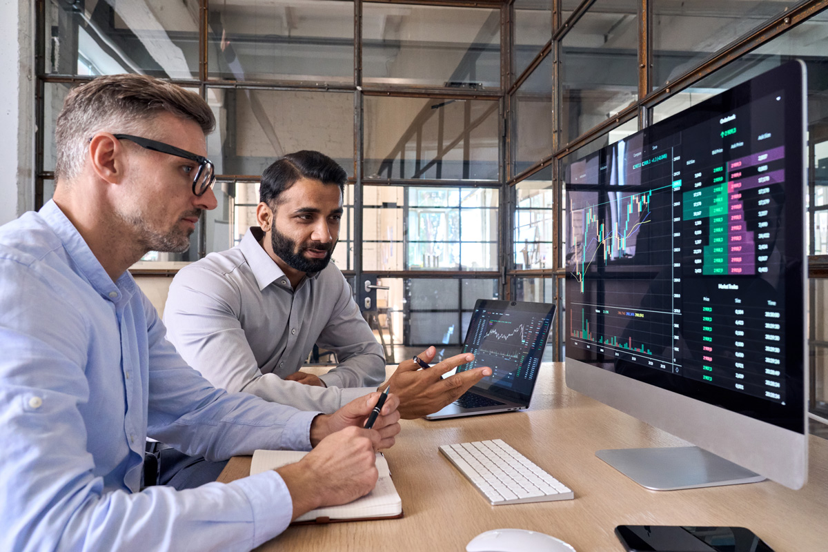 Two traders brokers stock exchange market investors discussing crypto trading charts growth using pc computer pointing at screen analyzing financial risks, investment profit forecast. Over shoulder