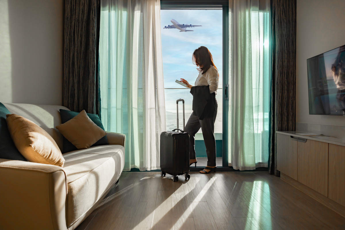 Woman with suitcase standing in home or hotel, online check-in in airline's mobile app or on the company's website for self-registration, obtaining boarding pass for quick access to flight at airport.